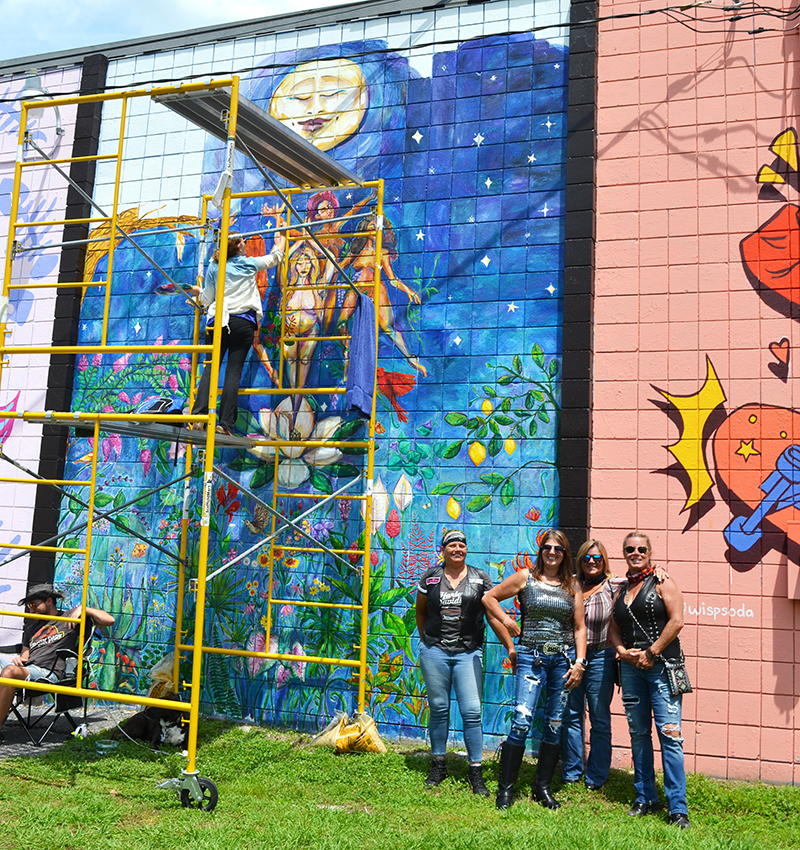 Here, a group of women riders pose in front of a mural being painted by a female artist.